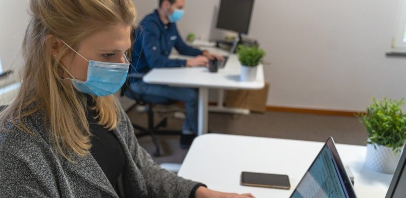 Woman wears mask at office desk during covid-19 pandemic